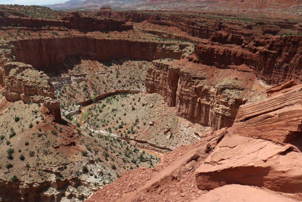 Deep red sandstone canyon in Capitol Reef National Park, Utah, with layered cliffs, desert vegetation, and a winding stream below.