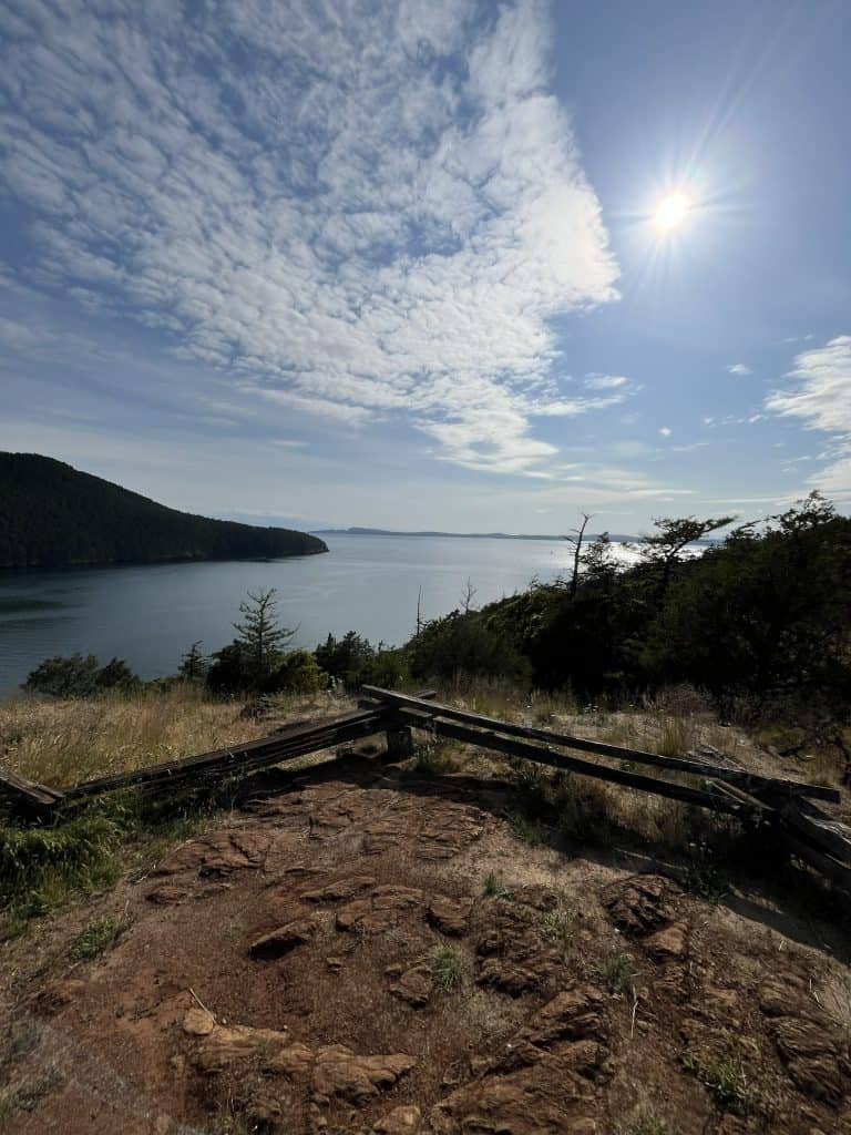 Scenic overlook on a nature hike in Anacortes, Washington, with coastal cliffs, blue sky, and sunlight reflecting over the Puget Sound.